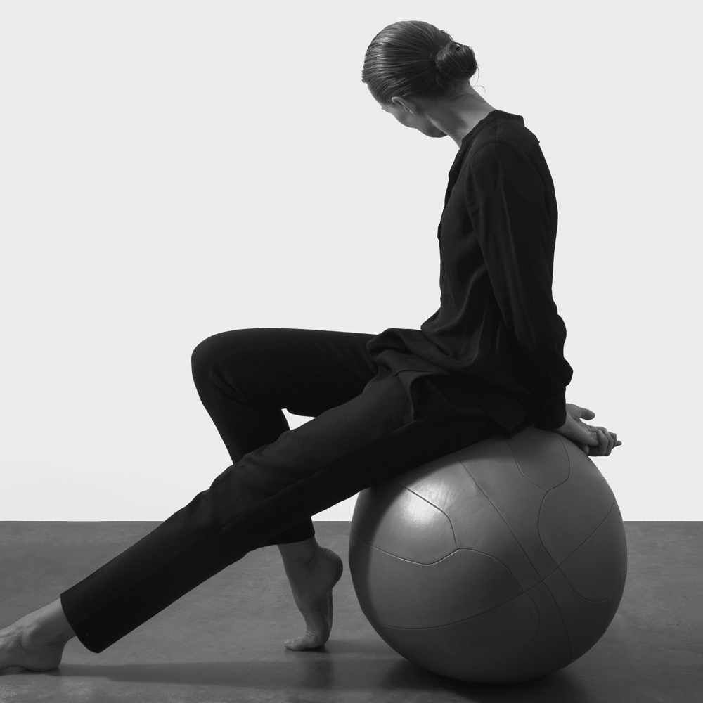 Woman wearing black sitting on an oval ball co-created with SPACE Copenhagen crafted in our NUANCE leather