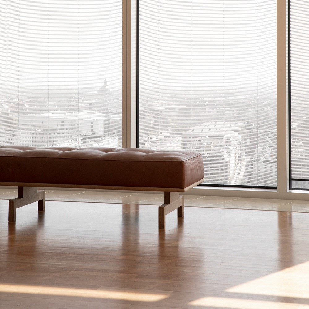 Brown leather daybed with wooden legs next to a window with a city view
